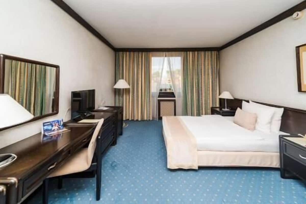 A hotel room with a bed, desk, chair, TV, and a view of a building through the window.