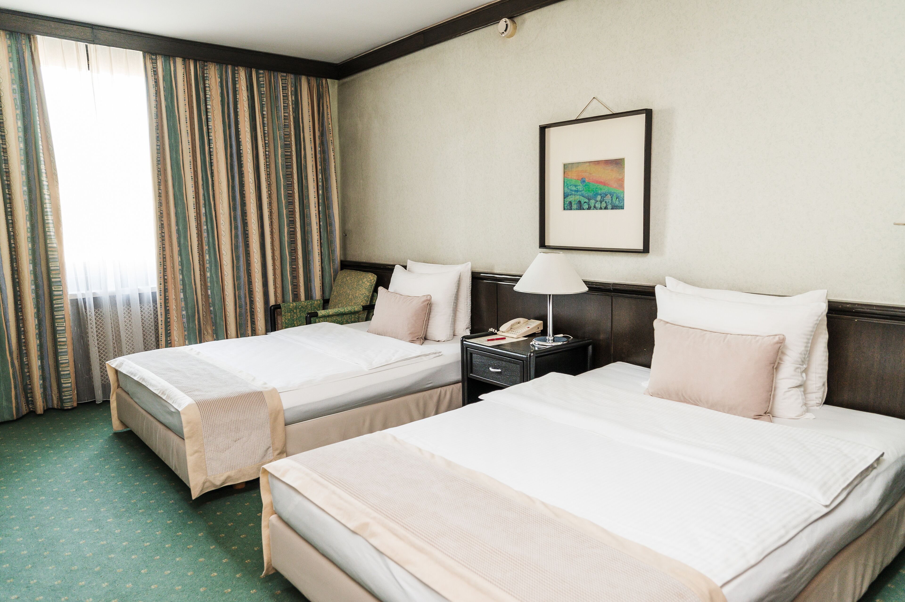 A hotel room with two beds, a nightstand with a lamp, a framed picture on the wall, and a window with curtains.