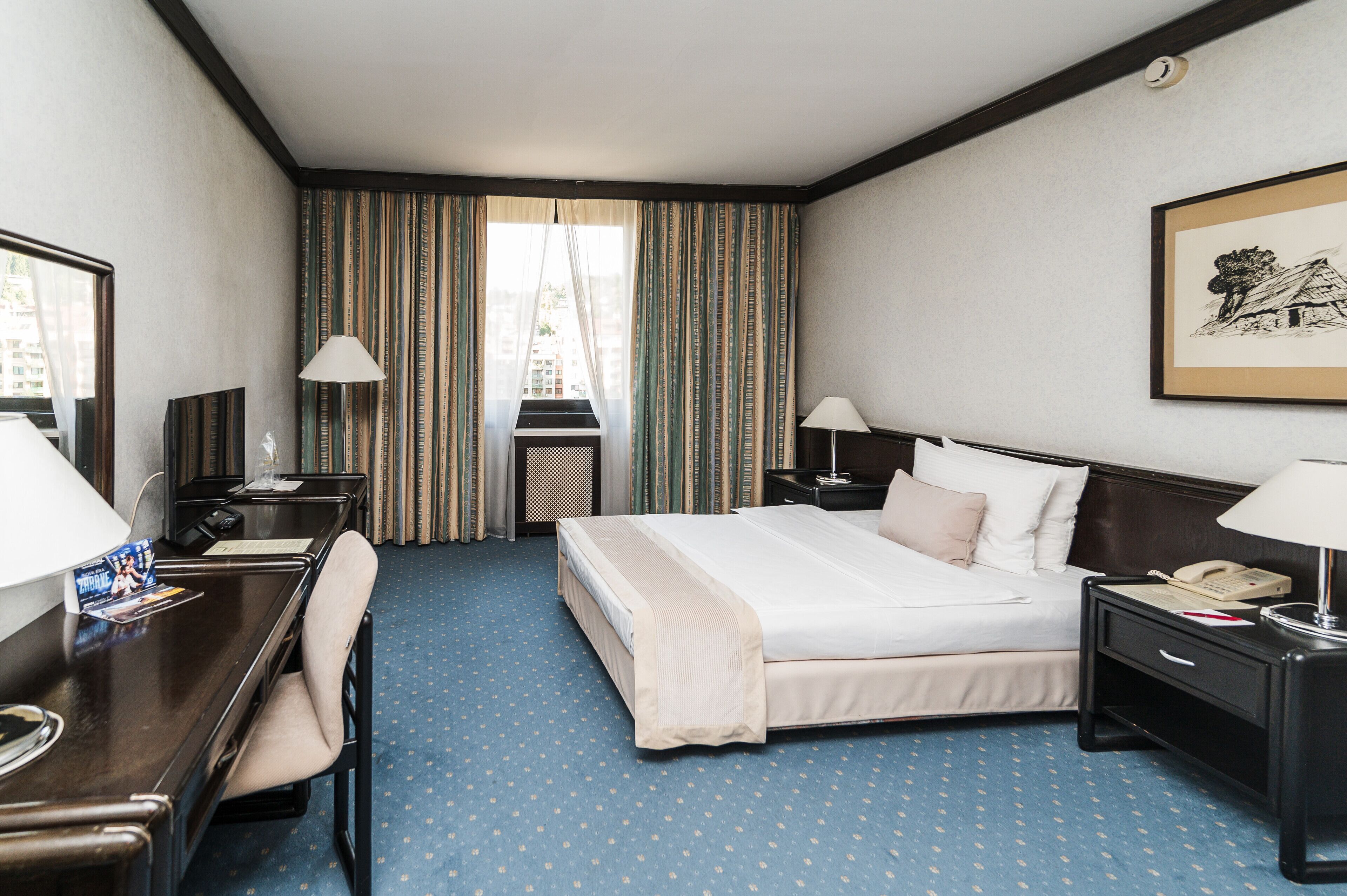 Habitación de hotel con cama, escritorio, silla y ventana con cortinas.