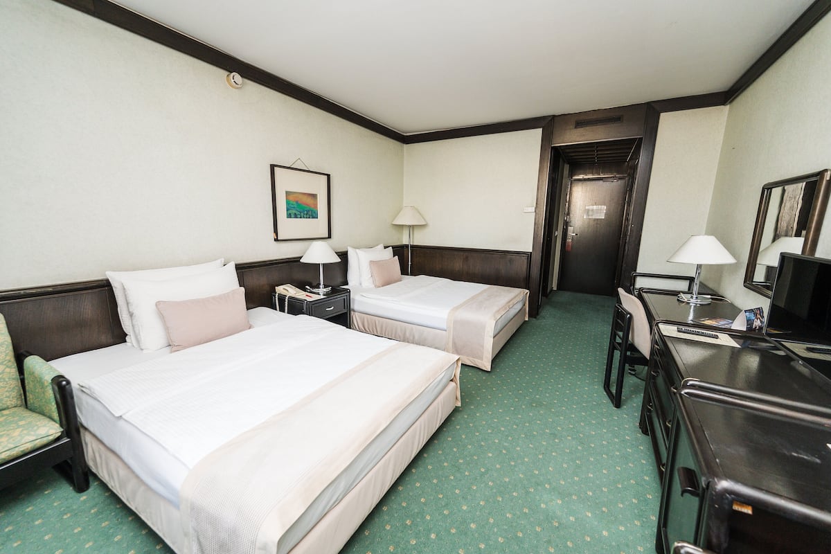 A hotel room with two beds, a desk, a chair, a lamp, and a picture on the wall.