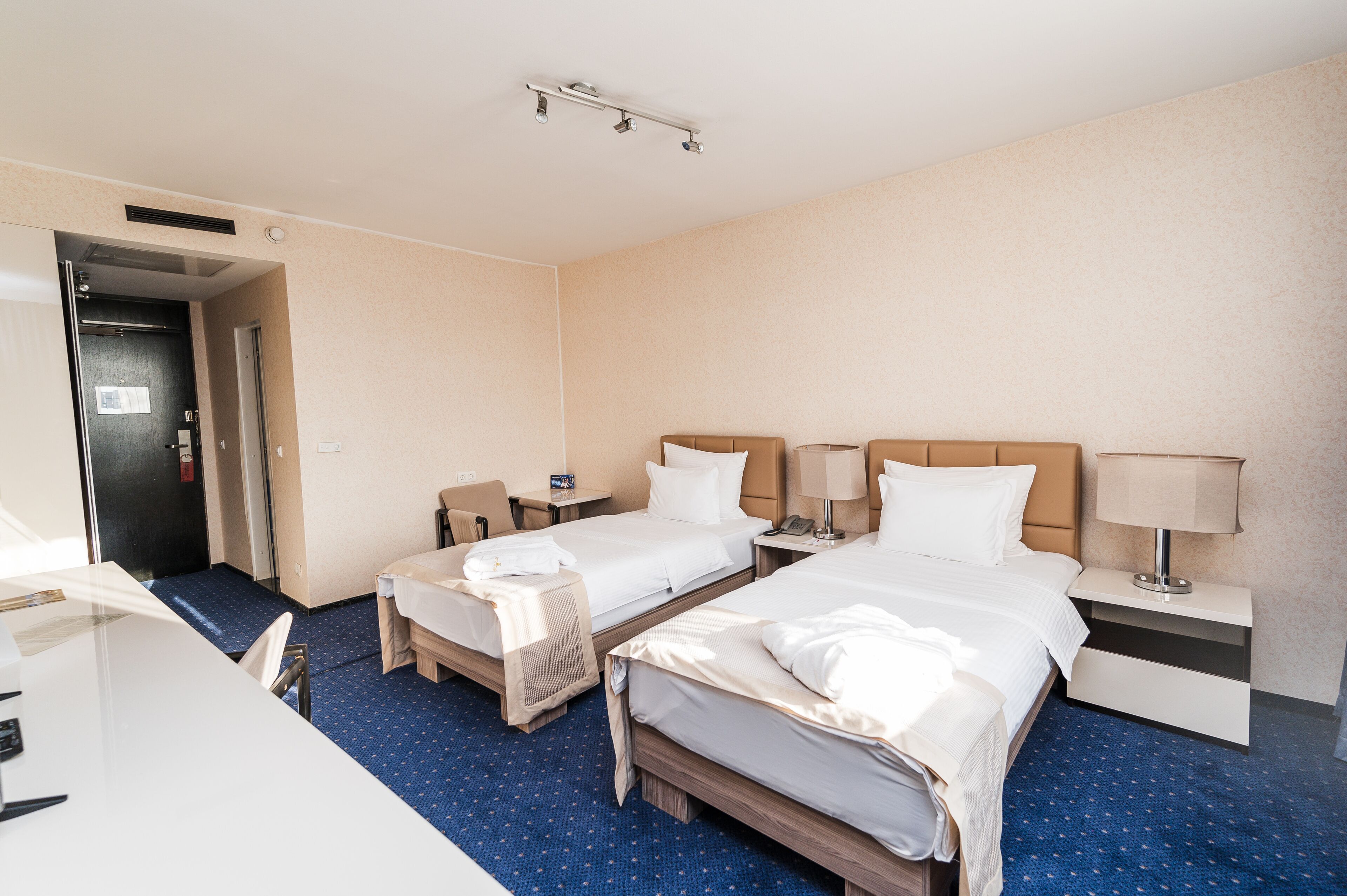 A hotel room with two beds, a desk, and a chair. There is a door to the left and a window on the right.