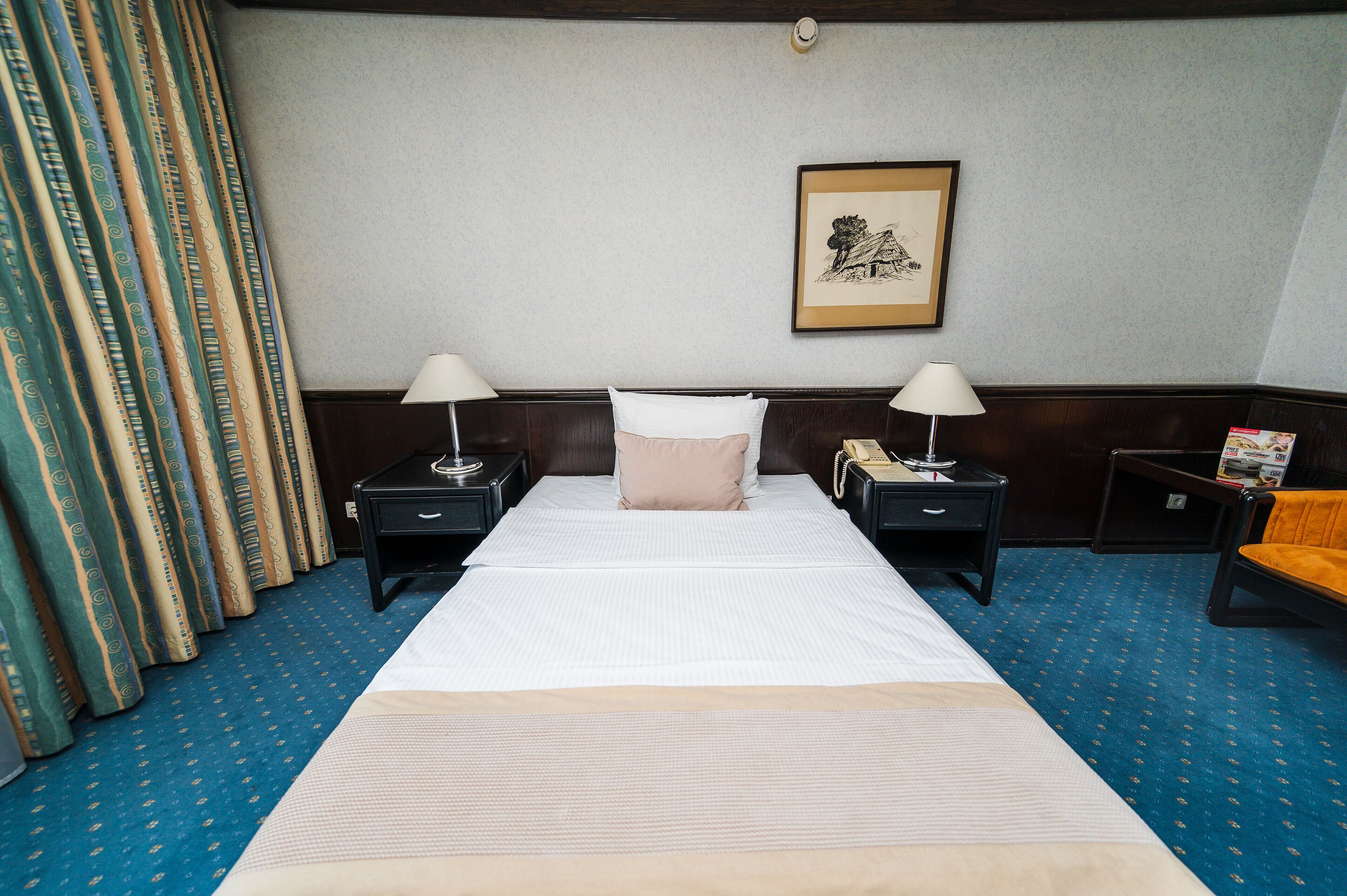 A hotel room with a large bed, two bedside tables with lamps, a framed picture on the wall, and a blue carpet.