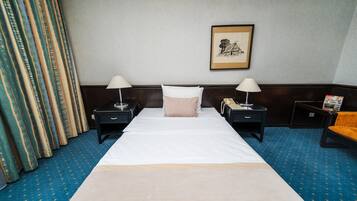 Habitación de hotel con una cama grande, dos mesitas de noche con lámparas, un cuadro enmarcado en la pared y una alfombra azul.