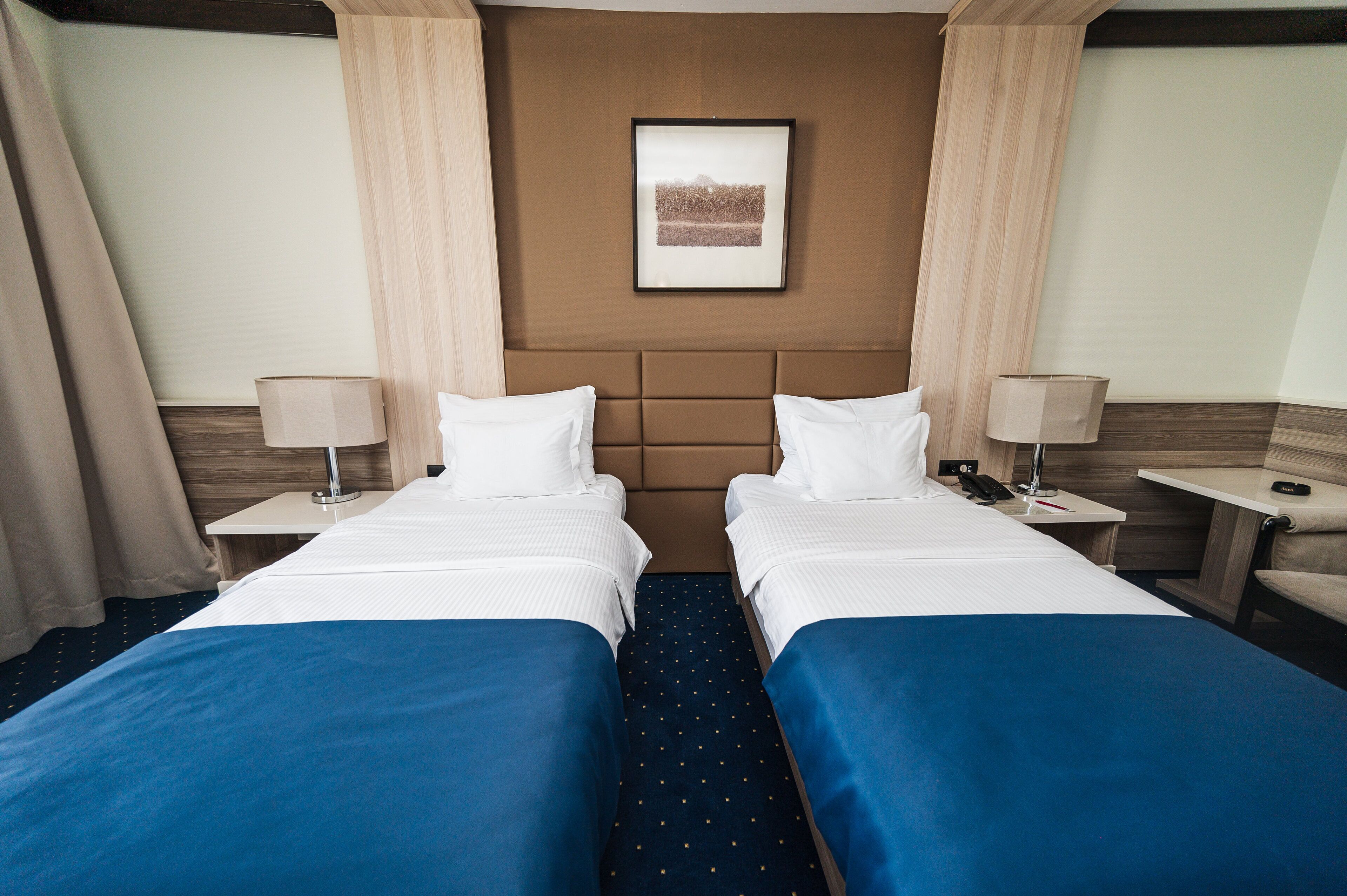 A hotel room with two beds, a headboard, a framed picture on the wall, and a nightstand with a lamp.