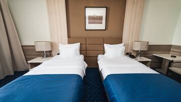 A hotel room with two beds, a headboard, a framed picture on the wall, and a nightstand with a lamp.
