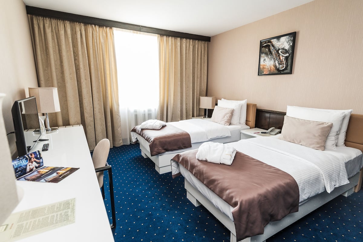 A hotel room with two beds, a desk, and a window with curtains.