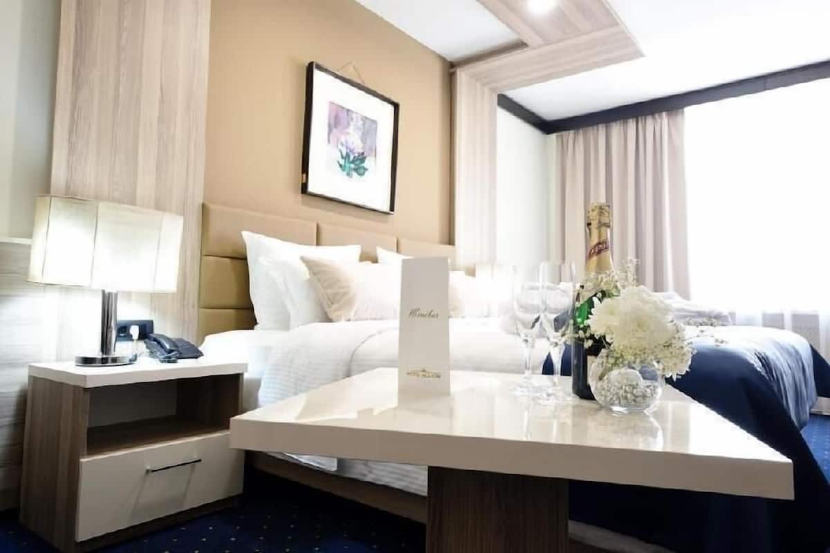 A hotel room with a bed, bedside table, lamp, and a vase with flowers.