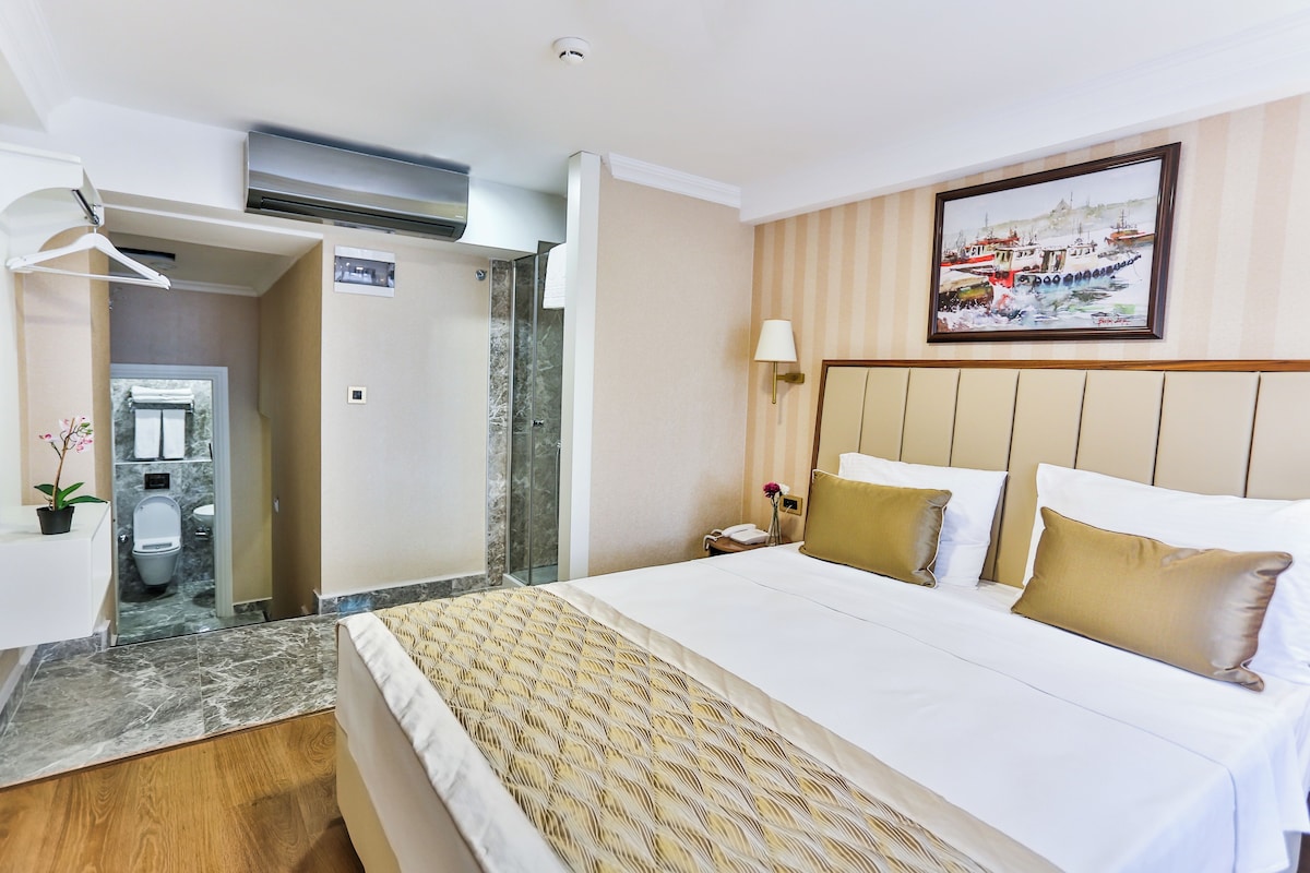 A hotel room with a large bed, a painting on the wall, and a bathroom visible through an open door.