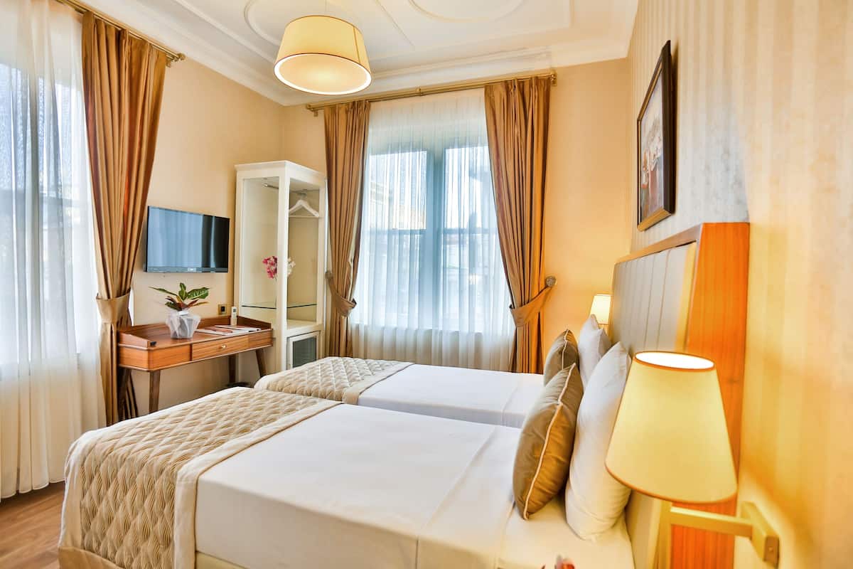 Ein Hotelzimmer mit zwei Betten, einem Schreibtisch mit Fernseher, einem Spiegel und einer Lampe.