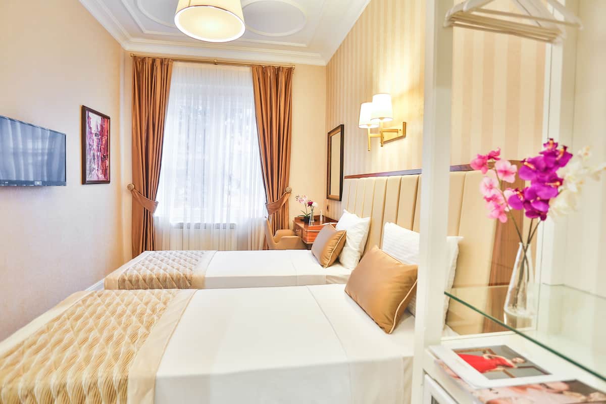Ein Hotelzimmer mit zwei Betten, einem Fernseher, einem Schreibtisch, einem Spiegel und einem Fenster mit Vorh ängen.