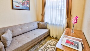 A living room with a sofa, a framed painting, a vase with flowers, and a magazine on a side table.