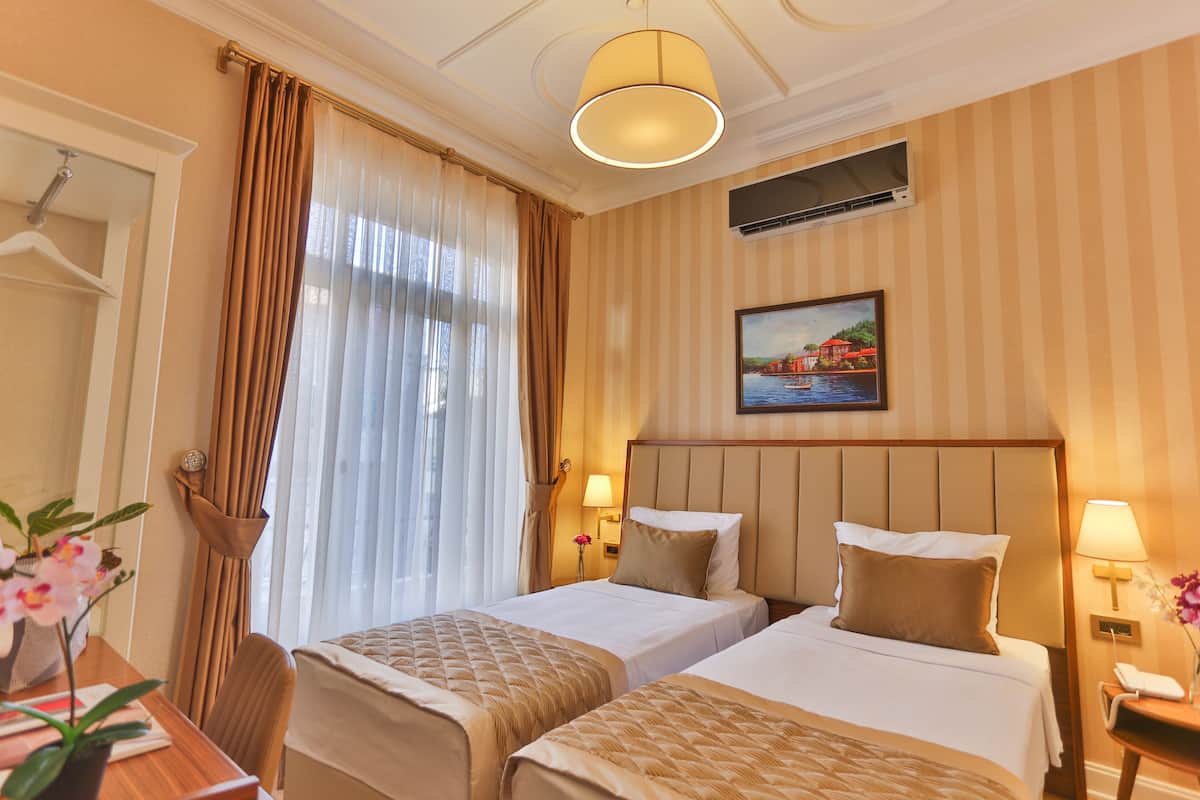Ein Hotelzimmer mit zwei Betten, einem Schreibtisch, einem Stuhl, einer Lampe und einem Bild an der Wand.