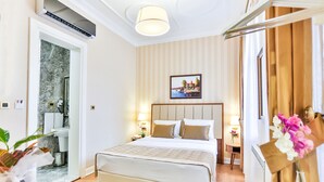 A hotel room with a large bed, a bathroom with a marble wall, and a picture of a coastal scene on the wall.