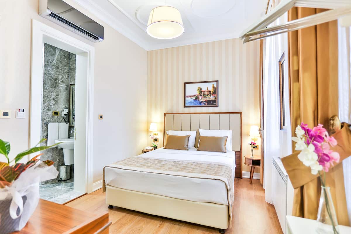 Ein Hotelzimmer mit einem großen Bett, einem Badezimmer mit Marmorwand und einem Bild einer Küstenlandschaft an der Wand.