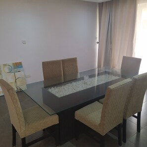 A dining area with a glass-top table surrounded by four chairs, a white textured rug, and a painting on the wall. - 21st century apartment (Lagos)