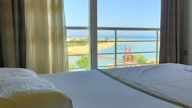 Una habitación de hotel con un ventanal que ofrece vistas a una playa y un puente.