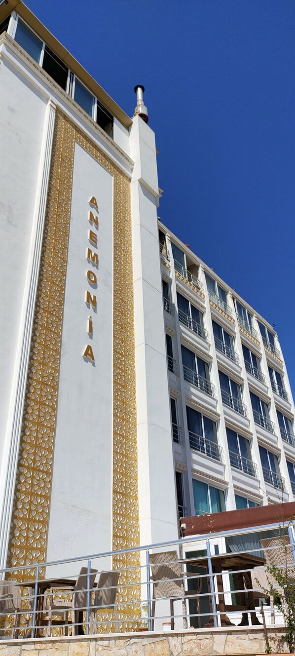 Un hotel de varios pisos con una fachada llamativa en dorado y blanco, que presenta un patrón vertical dorado y el nombre "ANEMONA" en el lateral.