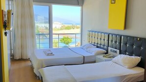 Habitación de hotel con dos camas, un ventanal con vista a la playa, una mesita de noche con un teléfono y una pared de acento amarillo.