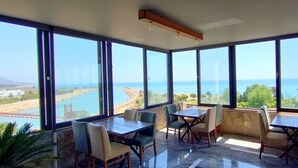 Un restaurante con grandes ventanales que ofrece vistas a la costa, incluyendo un puente y una playa.