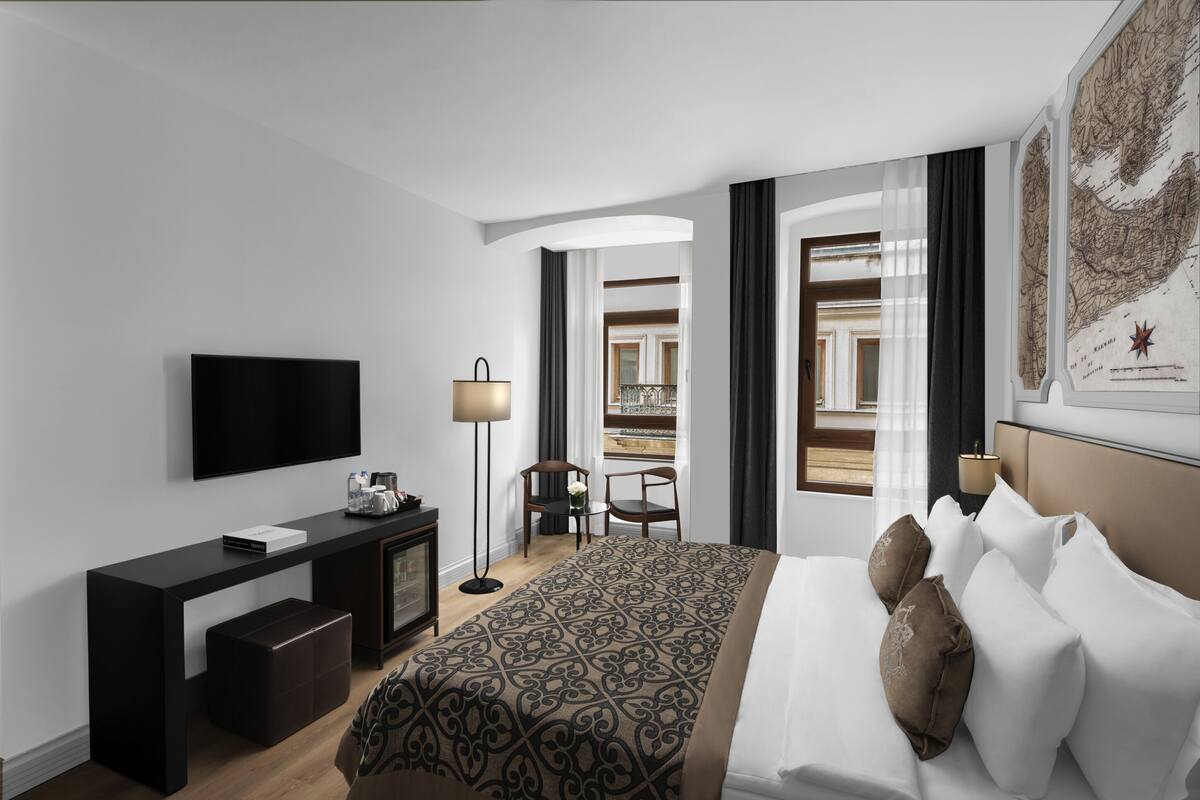 A hotel room with a bed, a desk, a TV, a chair, and a small table.