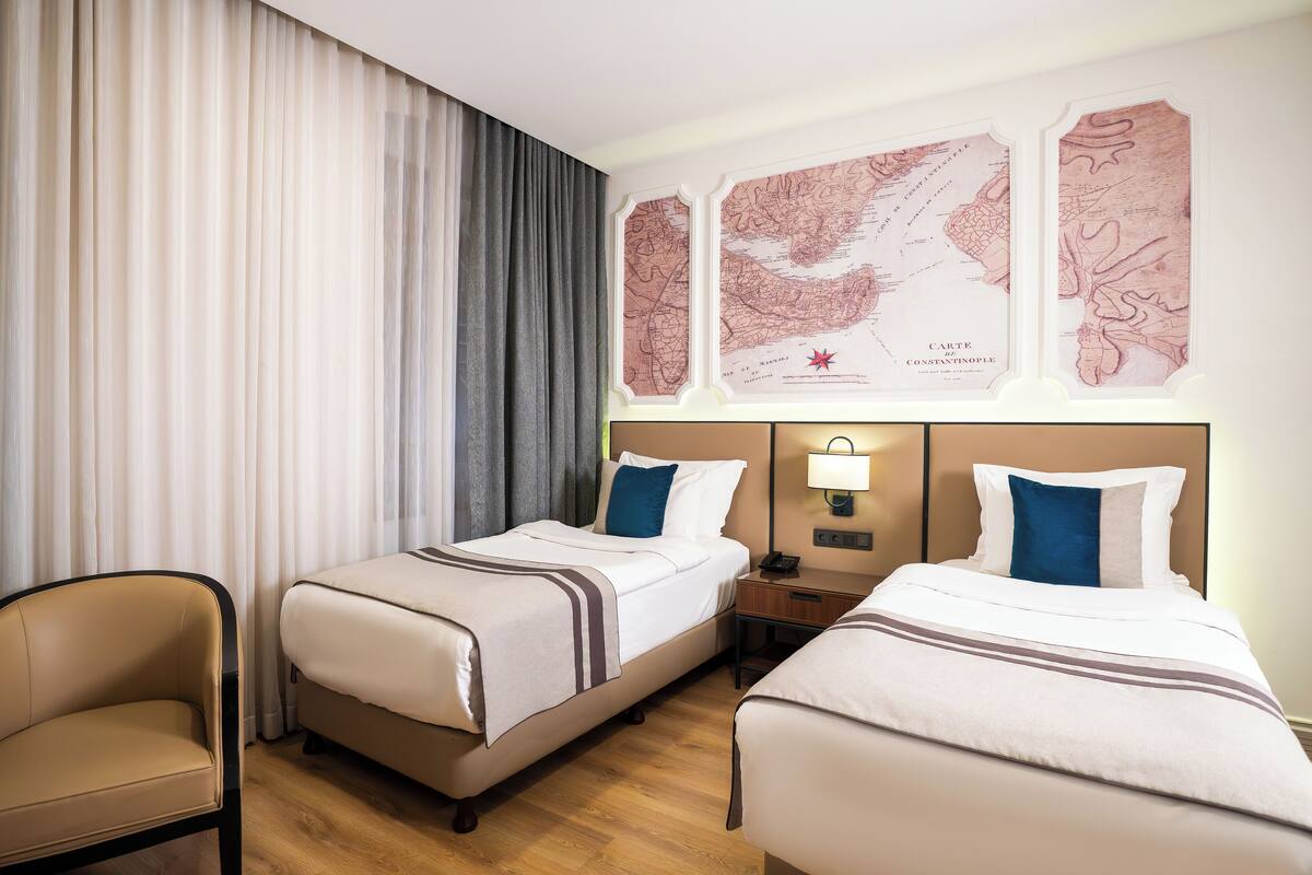 A hotel room with two beds, a desk, a chair, and a map on the wall.