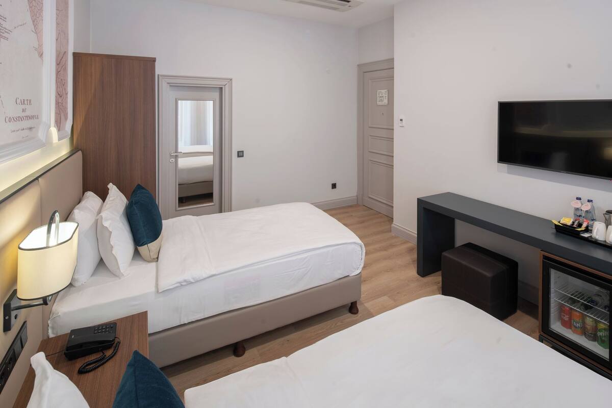 A hotel room with two beds, a desk, a television, and a minibar.