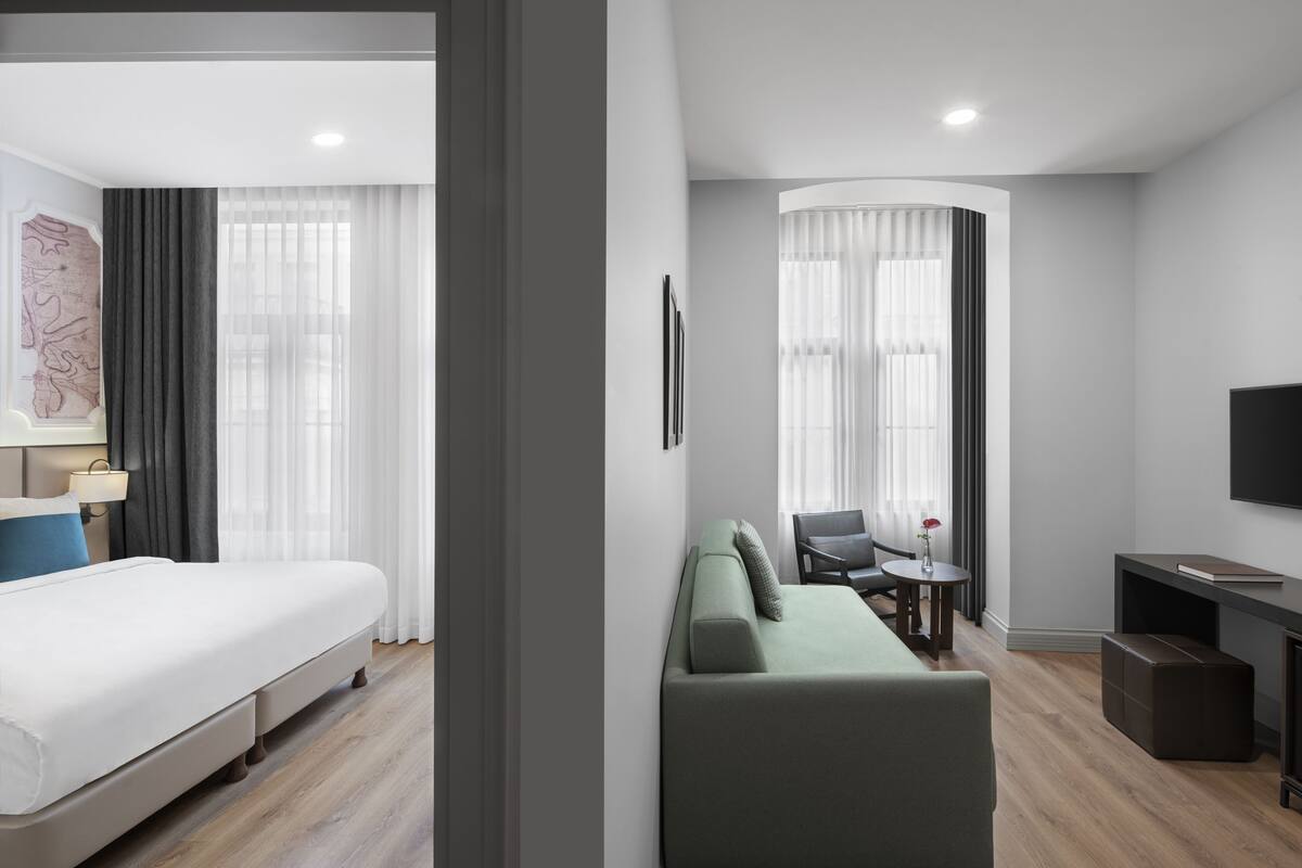 A modern hotel room with a bed, a green sofa, a small table, and a TV.