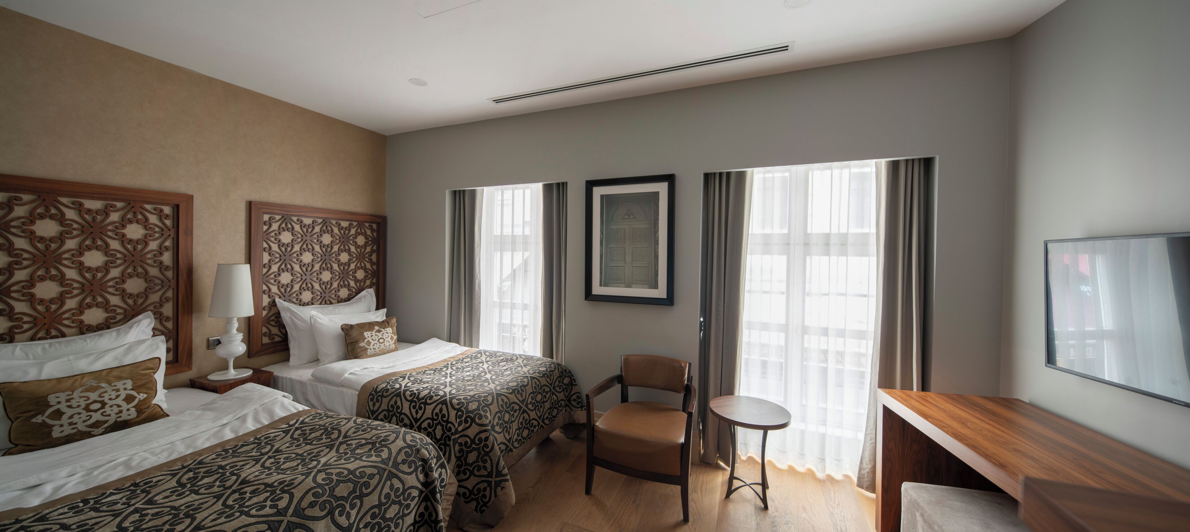 A hotel room with two beds, a chair, a small table, and a TV.