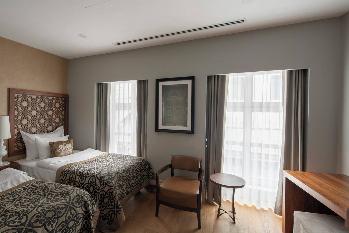 A hotel room with two beds, a chair, a small table, and a TV.