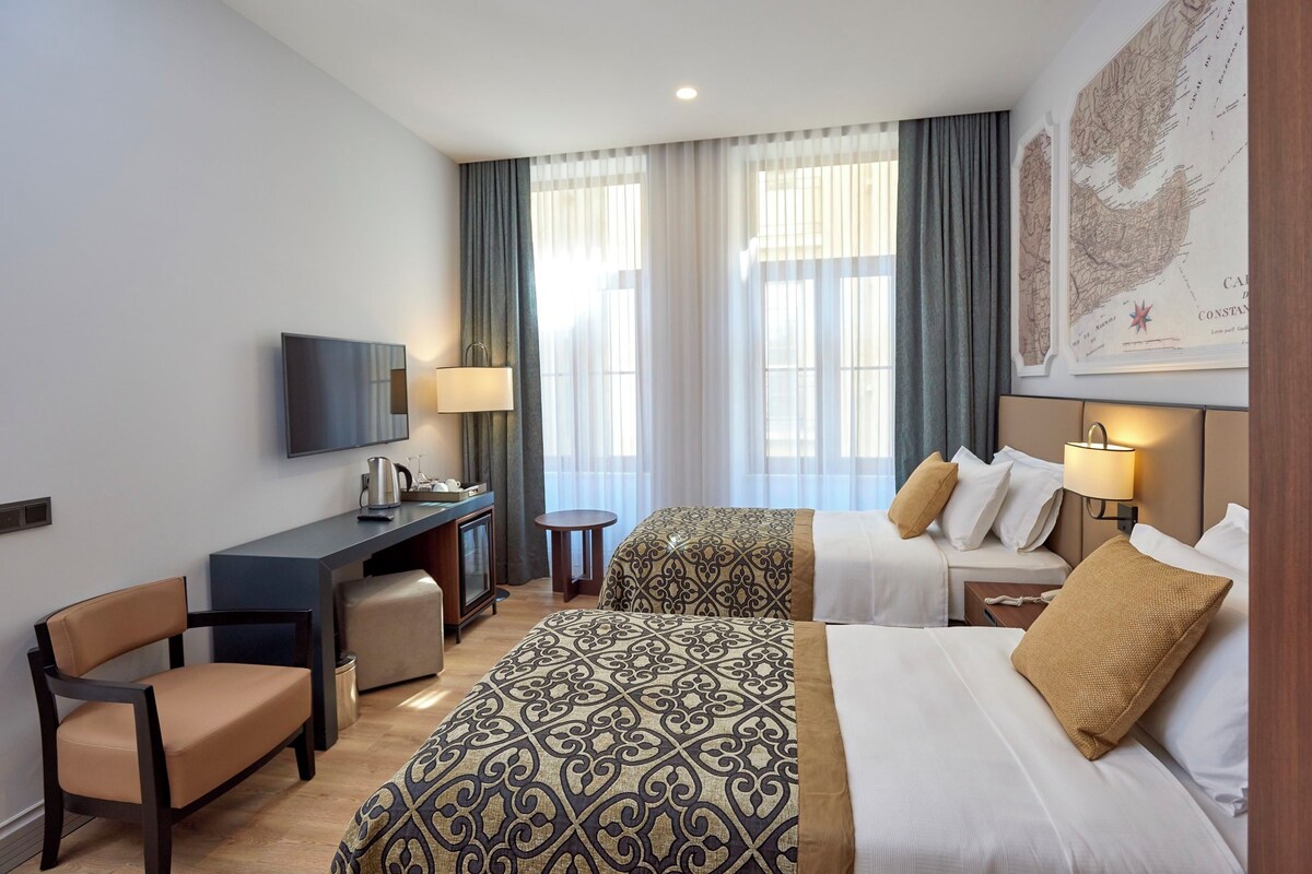 Une chambre d’hôtel avec deux lits, un bureau, une chaise, une télévision et une carte accrochée au mur.