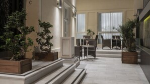 Un cortile interno moderno con area salotto, piante in vaso e una scala che conduce a un piano superiore.