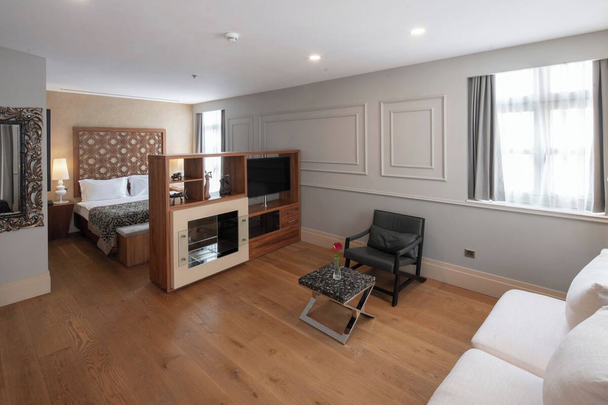 A hotel room with a bed, a TV, a small table, a chair, and a sofa.