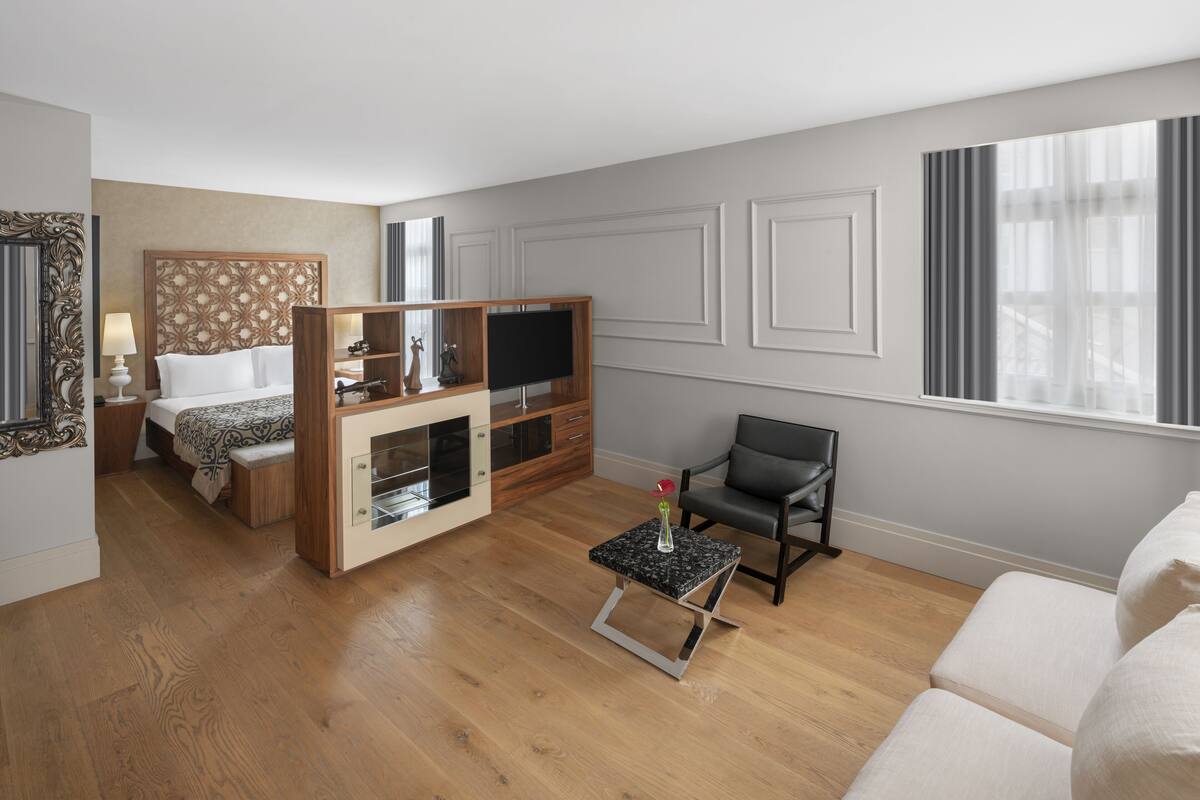 A hotel room with a bed, a TV, a small table with a vase, a sofa, and a chair.