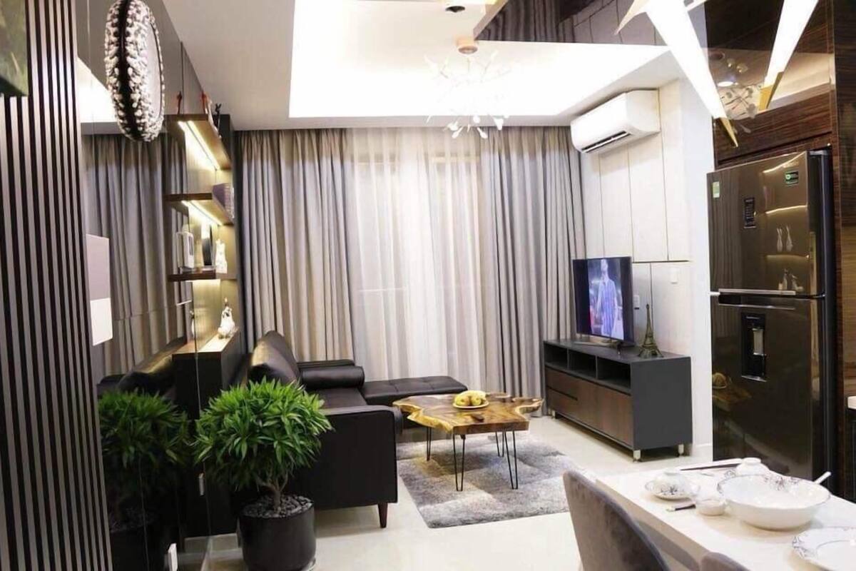 A modern living room with a sofa, coffee table, TV, and kitchen area with a refrigerator.