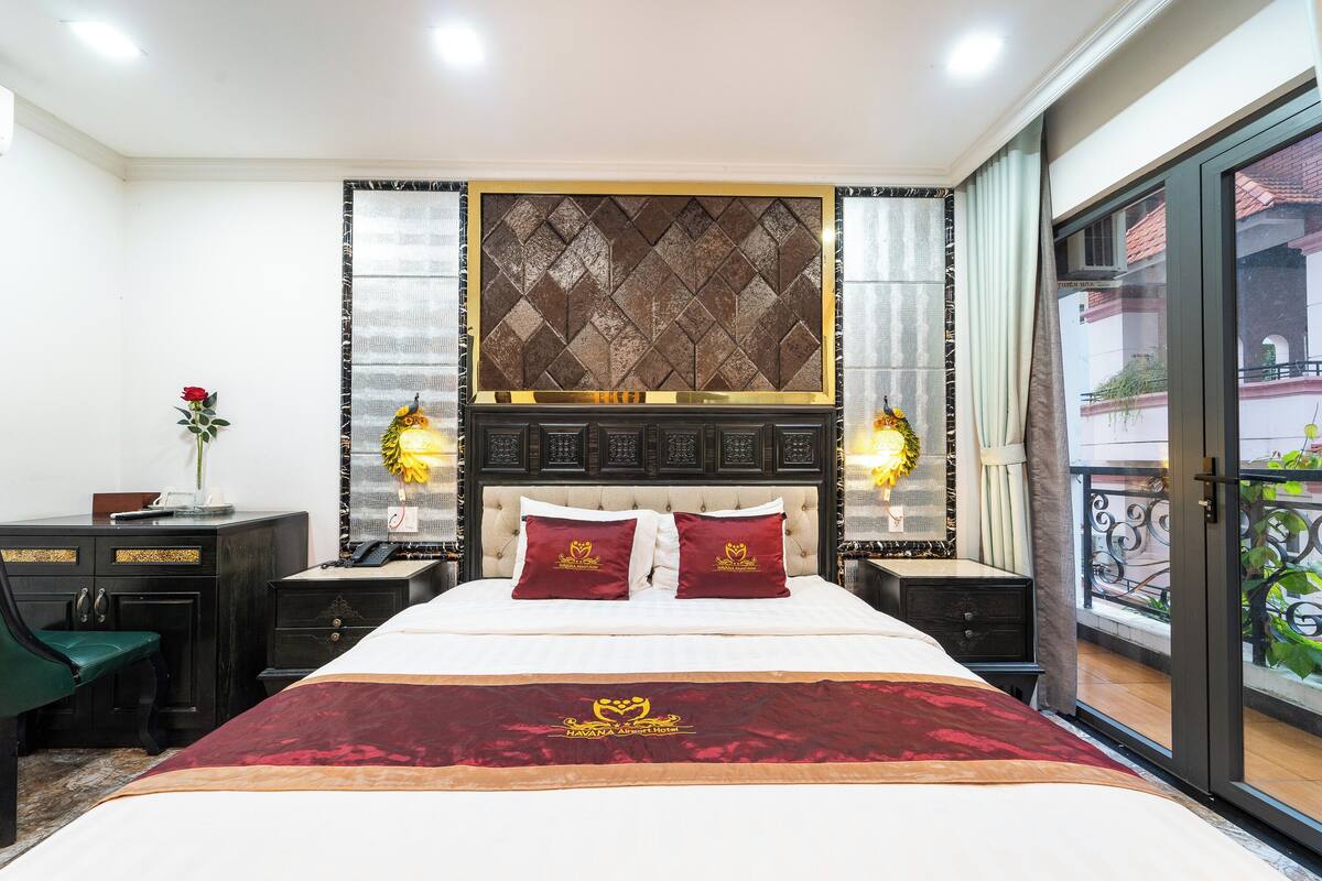 Une chambre d’hôtel avec un grand lit, une table de chevet, une commode et une vue sur le balcon extérieur.
