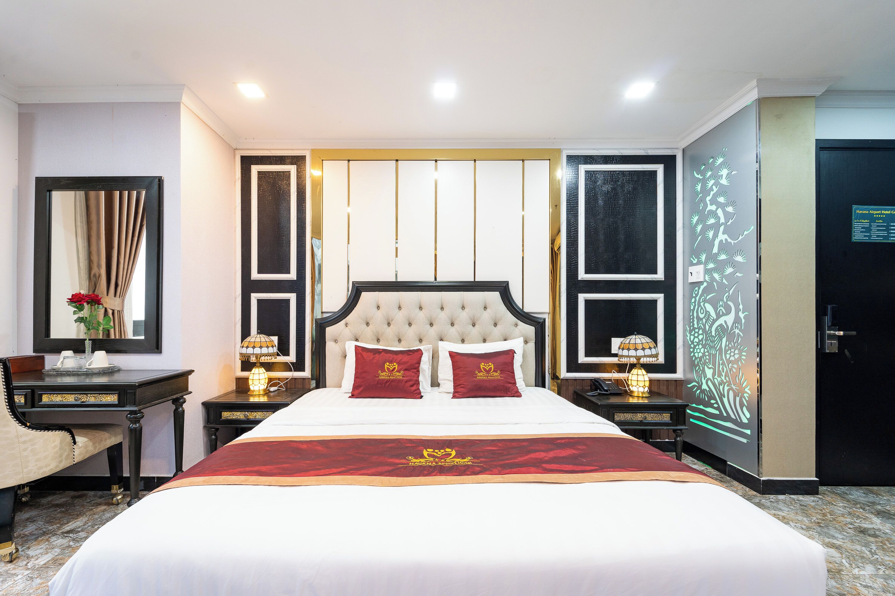 A hotel room with a large bed, two bedside tables with lamps, a mirror, and a decorative wall panel.