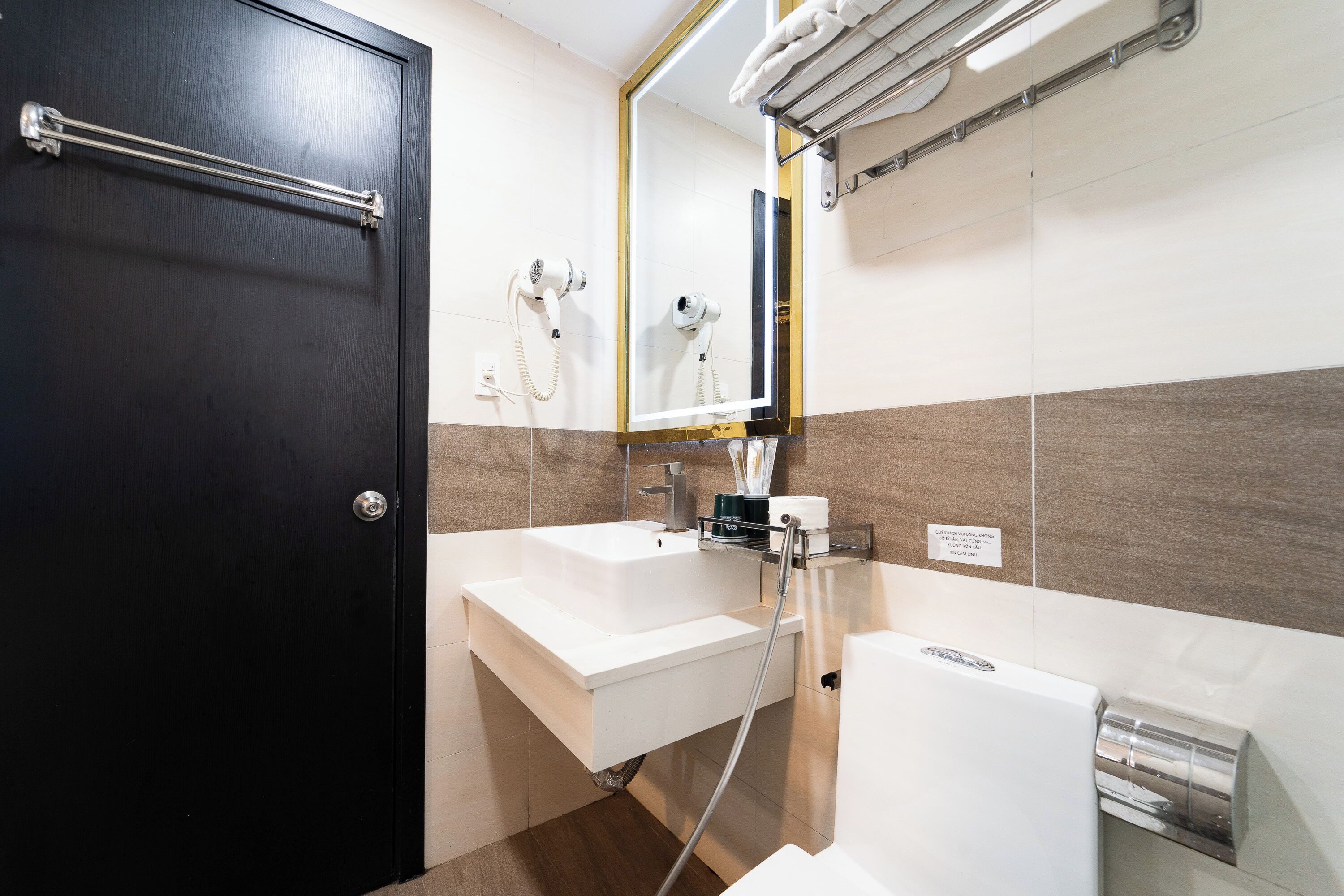 A modern bathroom with a dark door, a white sink, a mirror, and a towel rack.