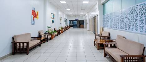 A long corridor with wooden benches and potted plants, leading to a reception area.