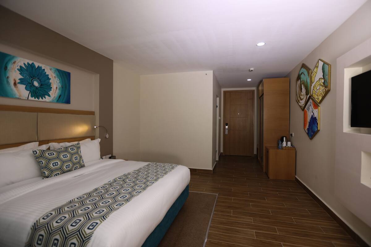 Une chambre d’hôtel avec un grand lit, une tête de lit, un téléviseur fixé au mur et des œuvres d’art.