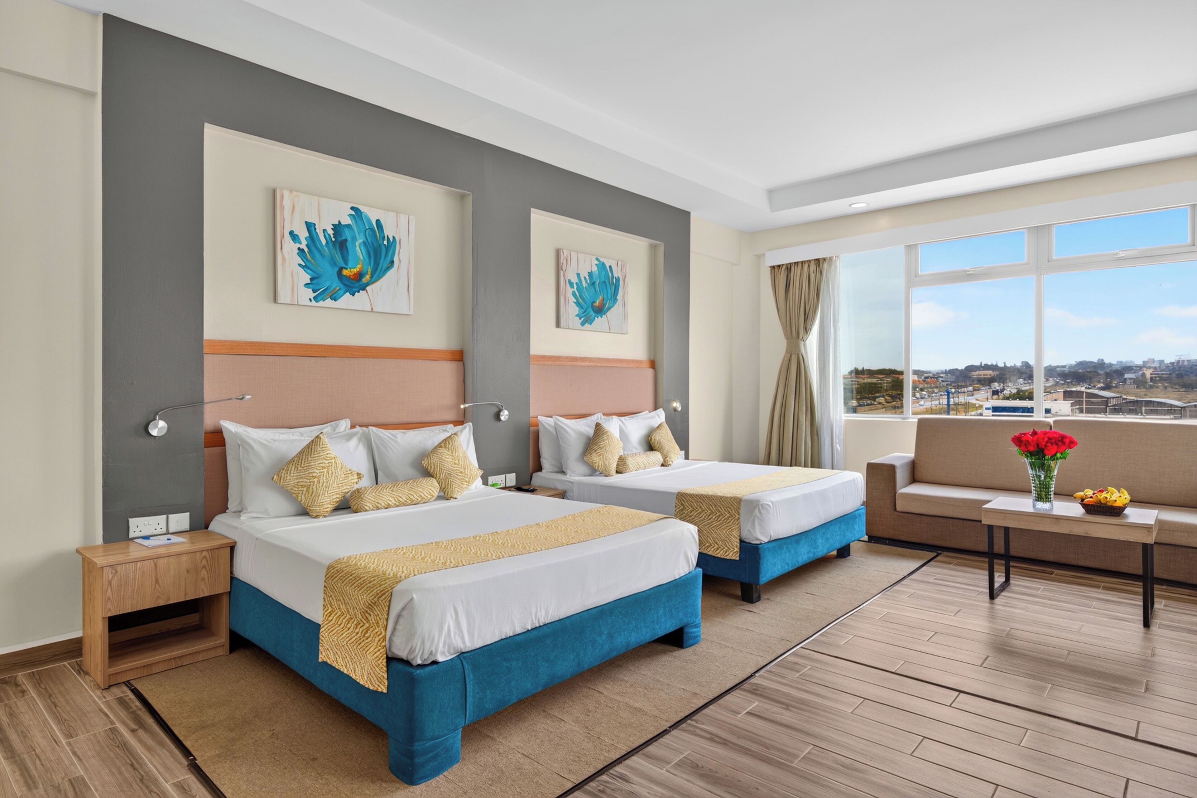 Habitación de hotel con dos camas, un sofá, una mesita y un ventanal con vistas a la ciudad.