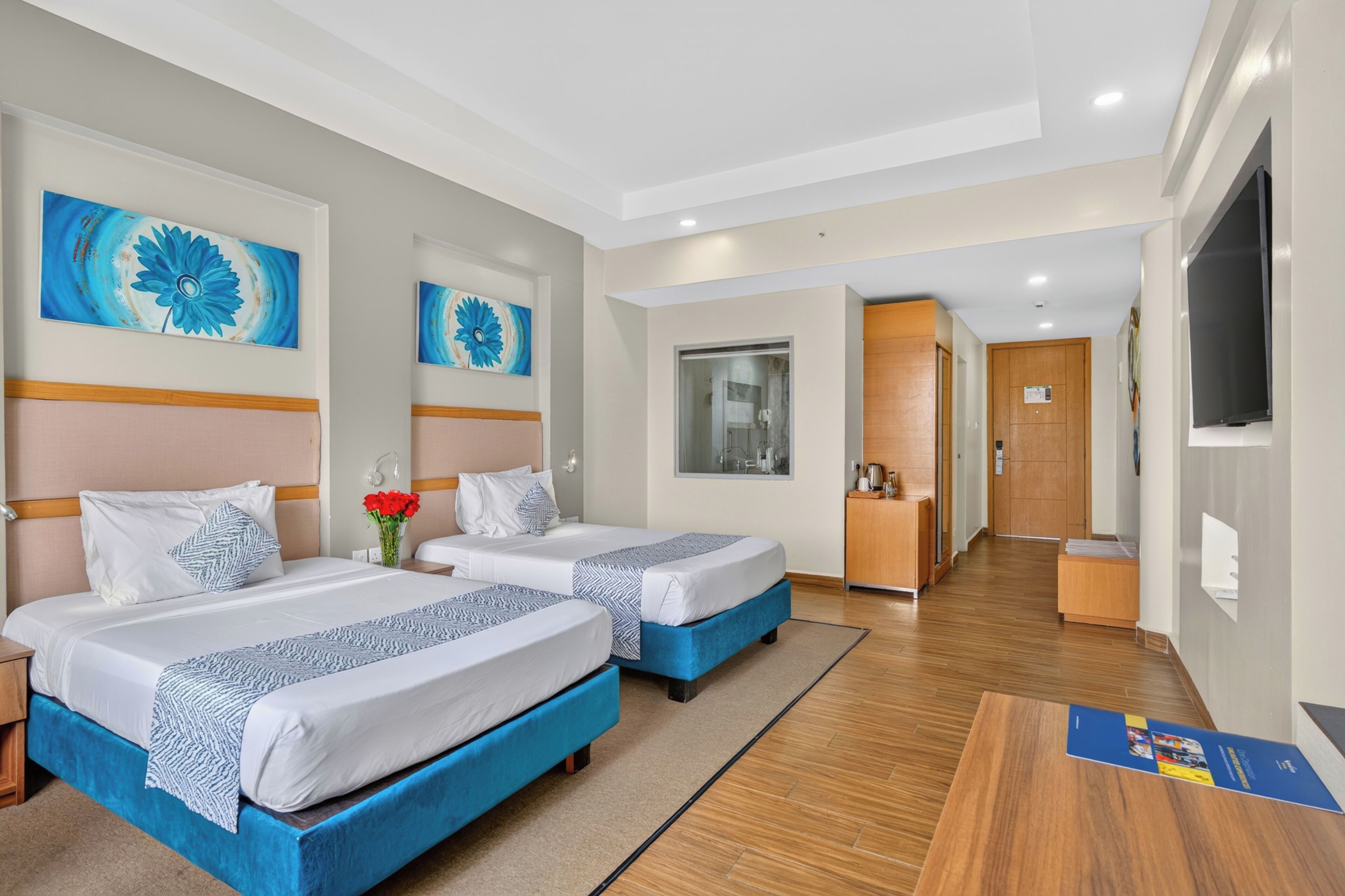 A hotel room with two beds, a bathroom, a kitchenette, and a TV.