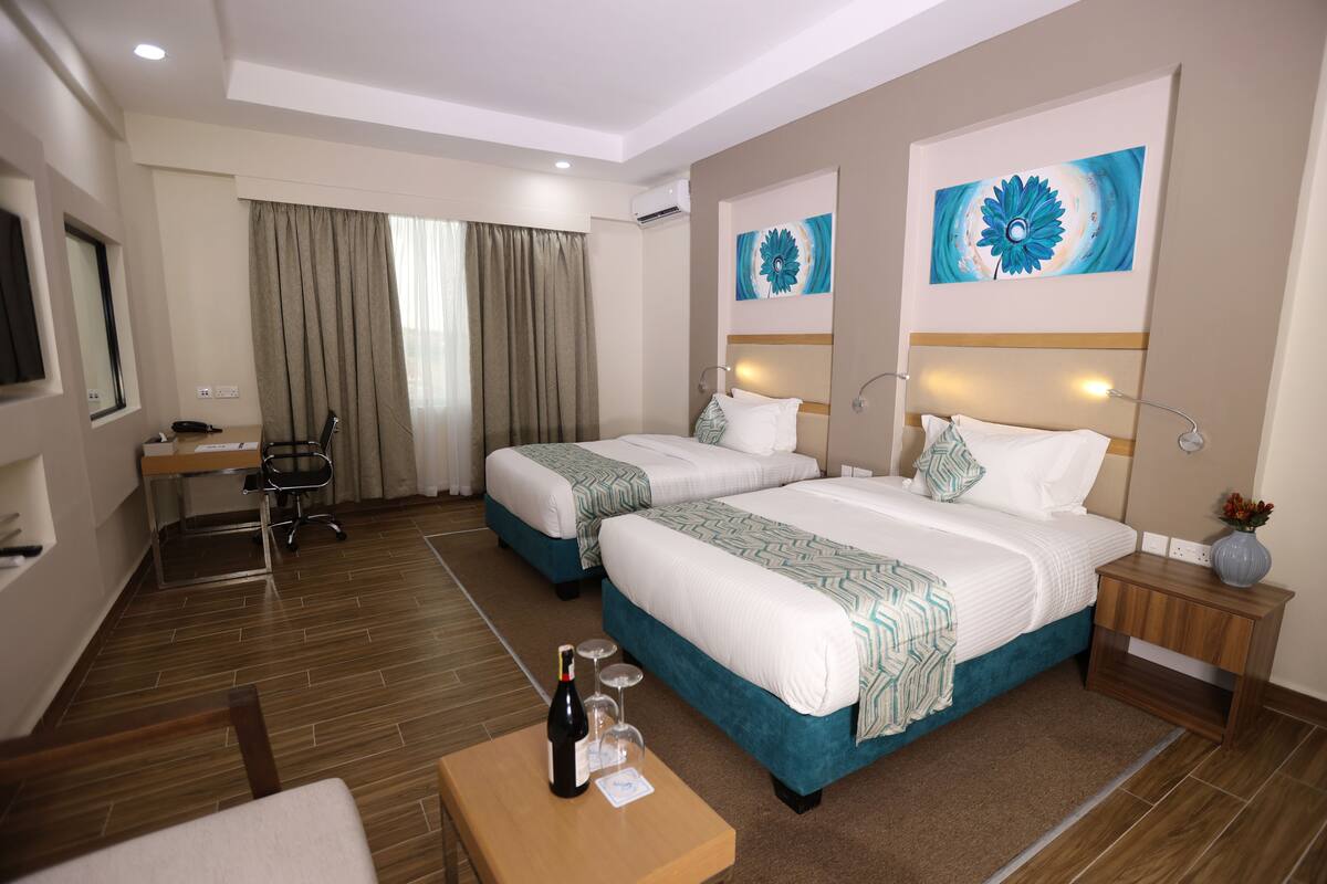 Une chambre d’hôtel avec deux lits, un bureau et une chaise. Il y a une bouteille et des verres sur le bureau.