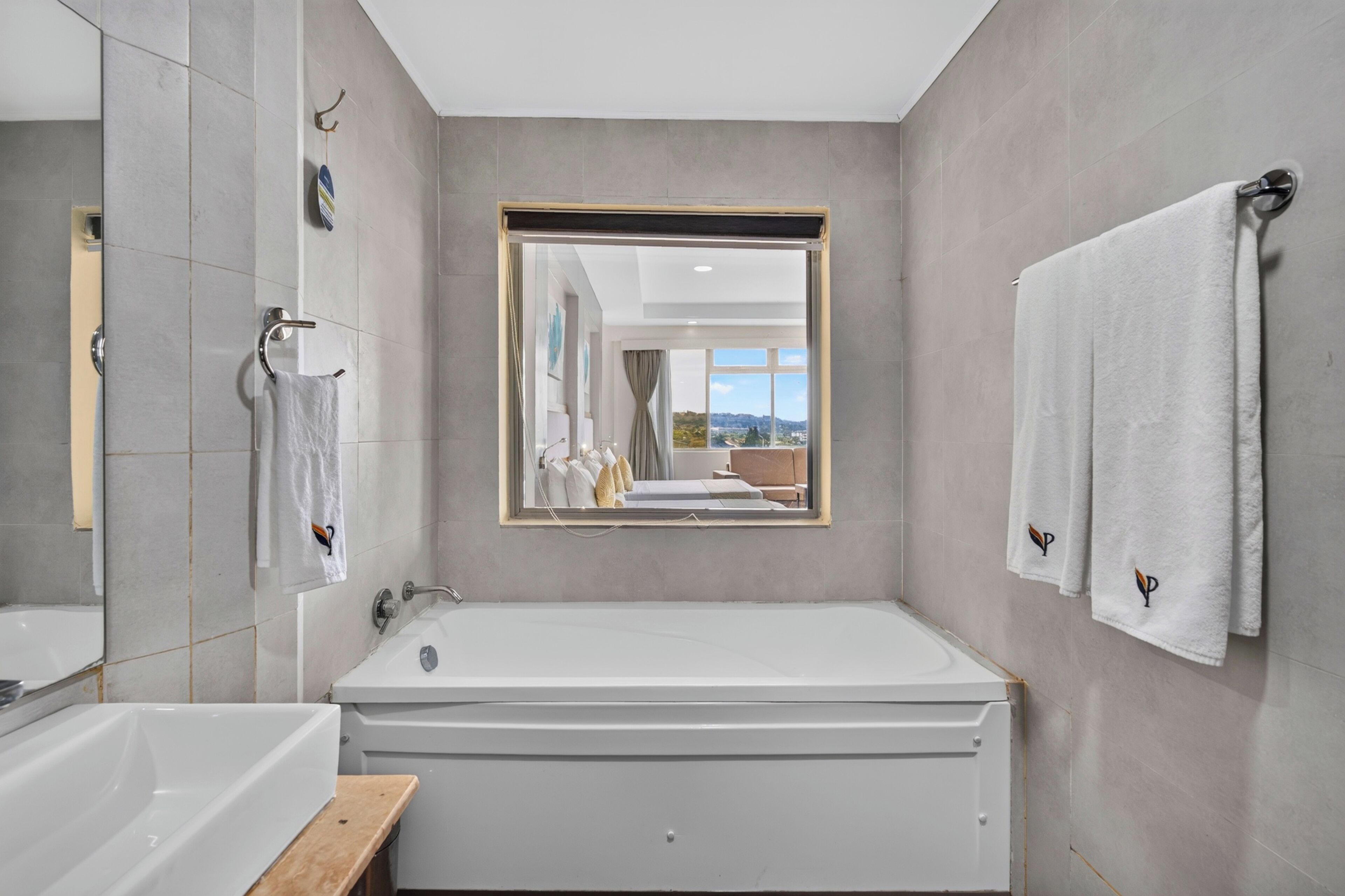 A modern bathroom with a large bathtub, a mirror, and two towels hanging on hooks.