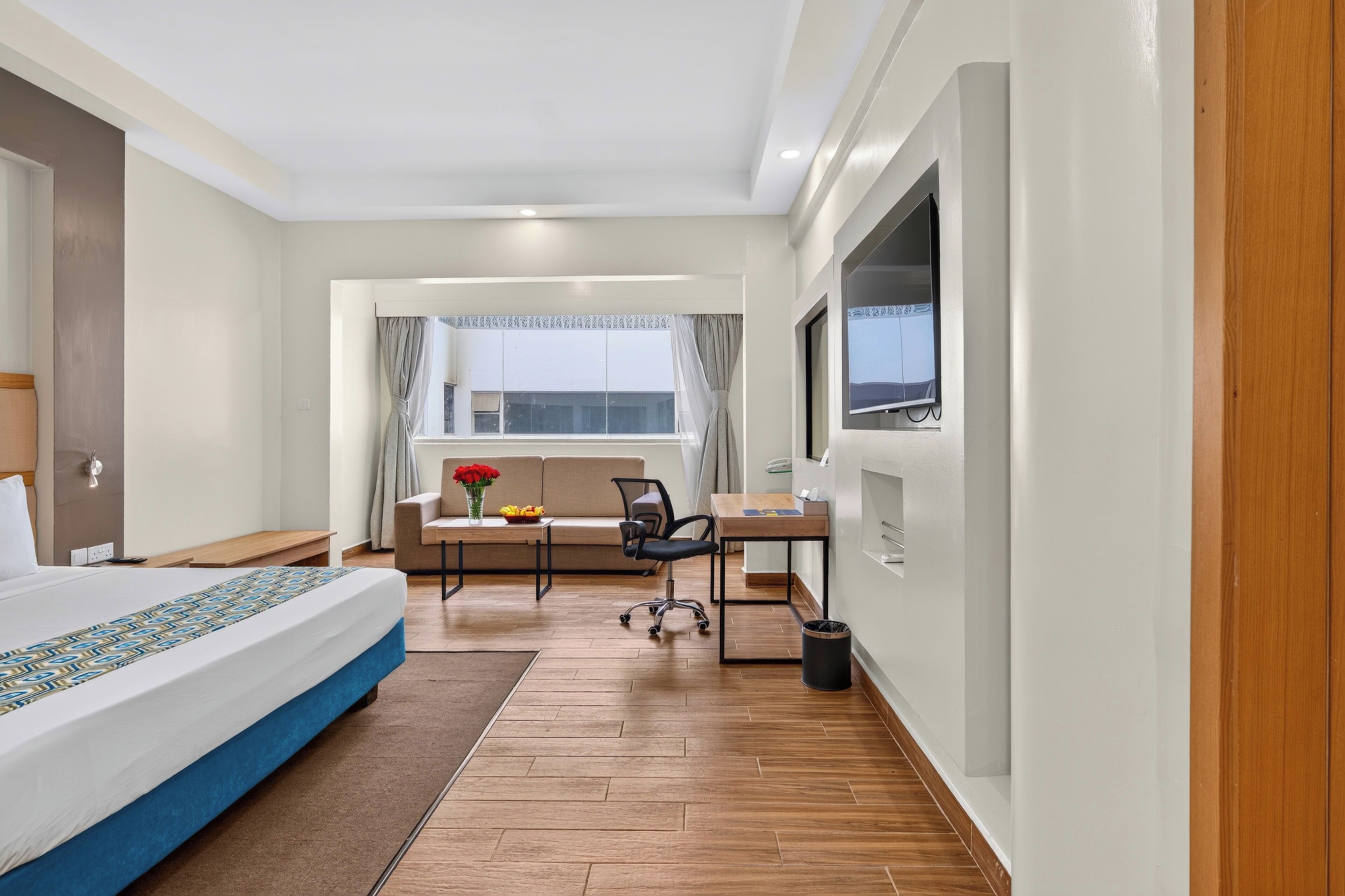 A hotel room with a bed, a desk, a chair, a TV, and a window with curtains.