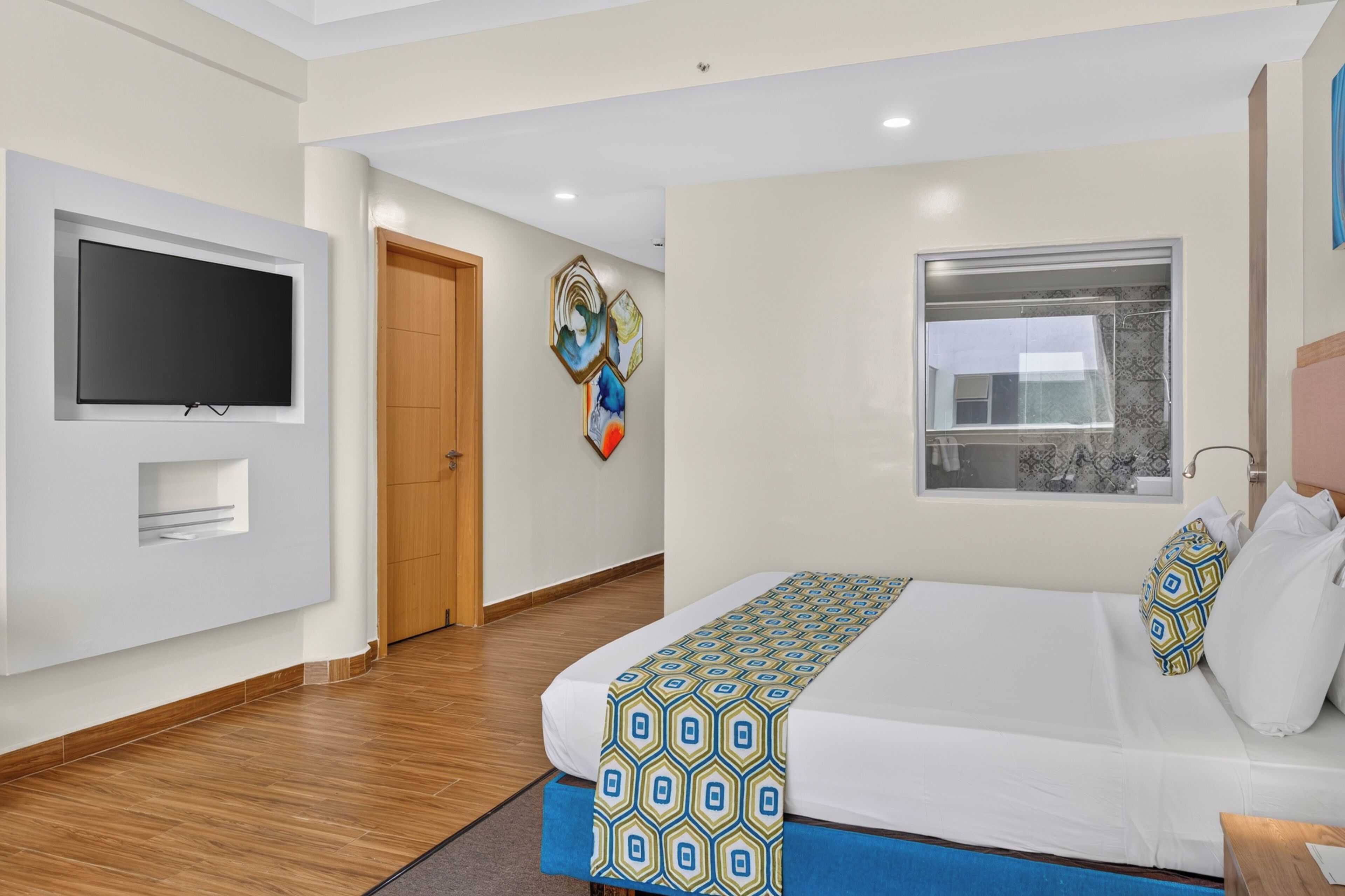 A hotel room with a bed, a television, a window, and artwork on the wall.