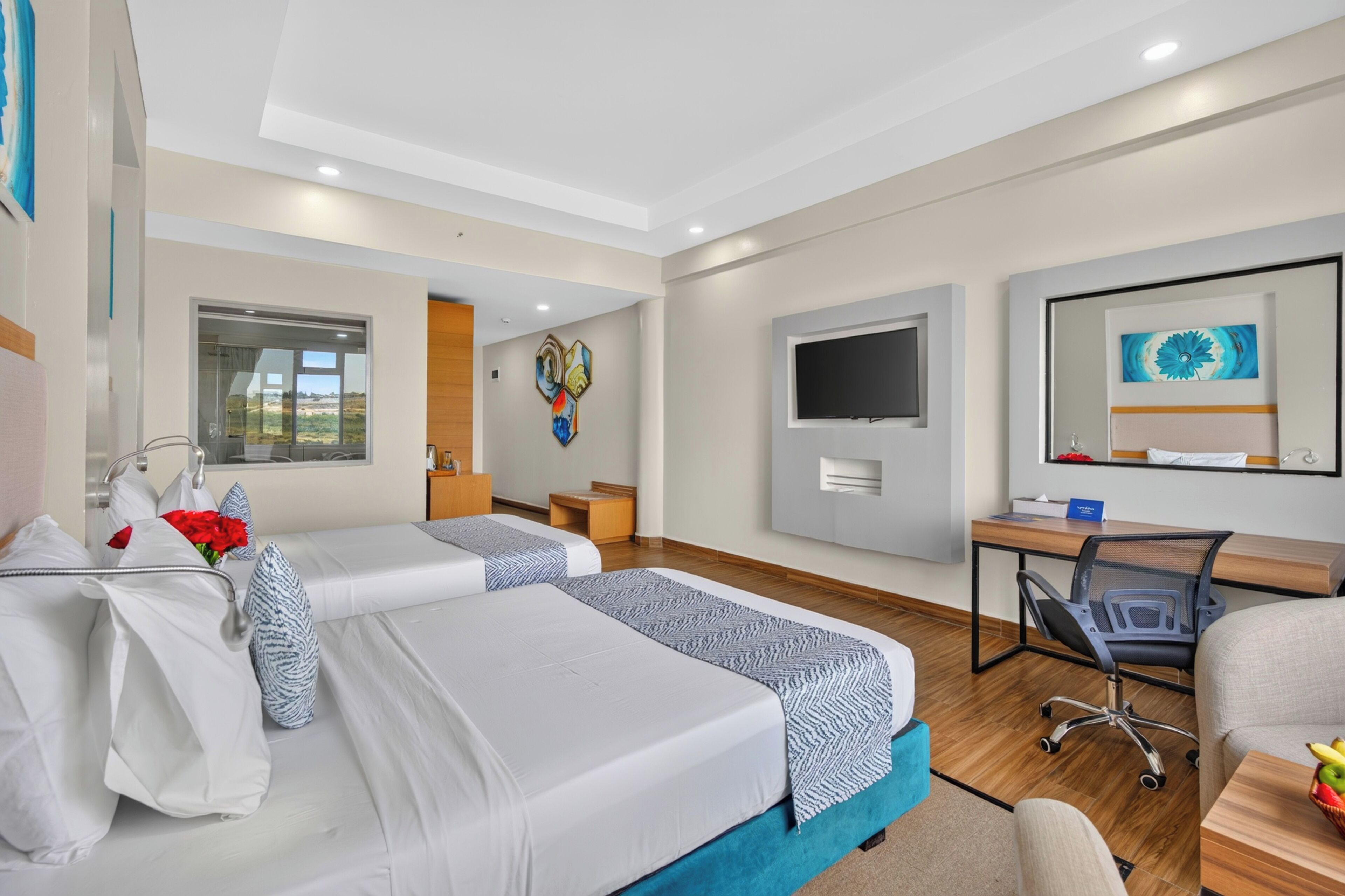 A hotel room with two beds, a desk, a chair, a TV, and a window with a view.