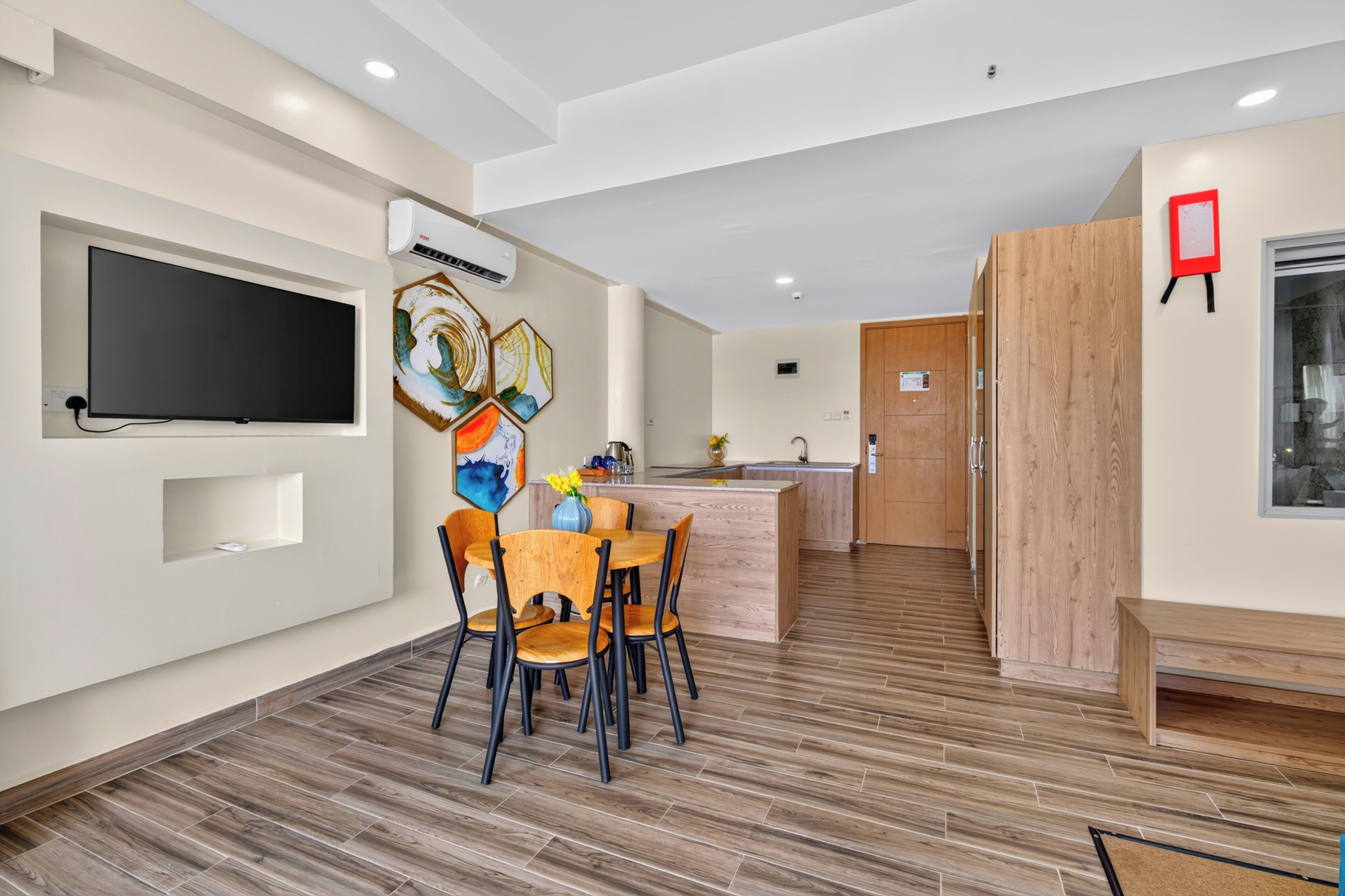 A modern kitchen with a central island, a dining area with wooden chairs, and a flat-screen TV mounted on the wall.