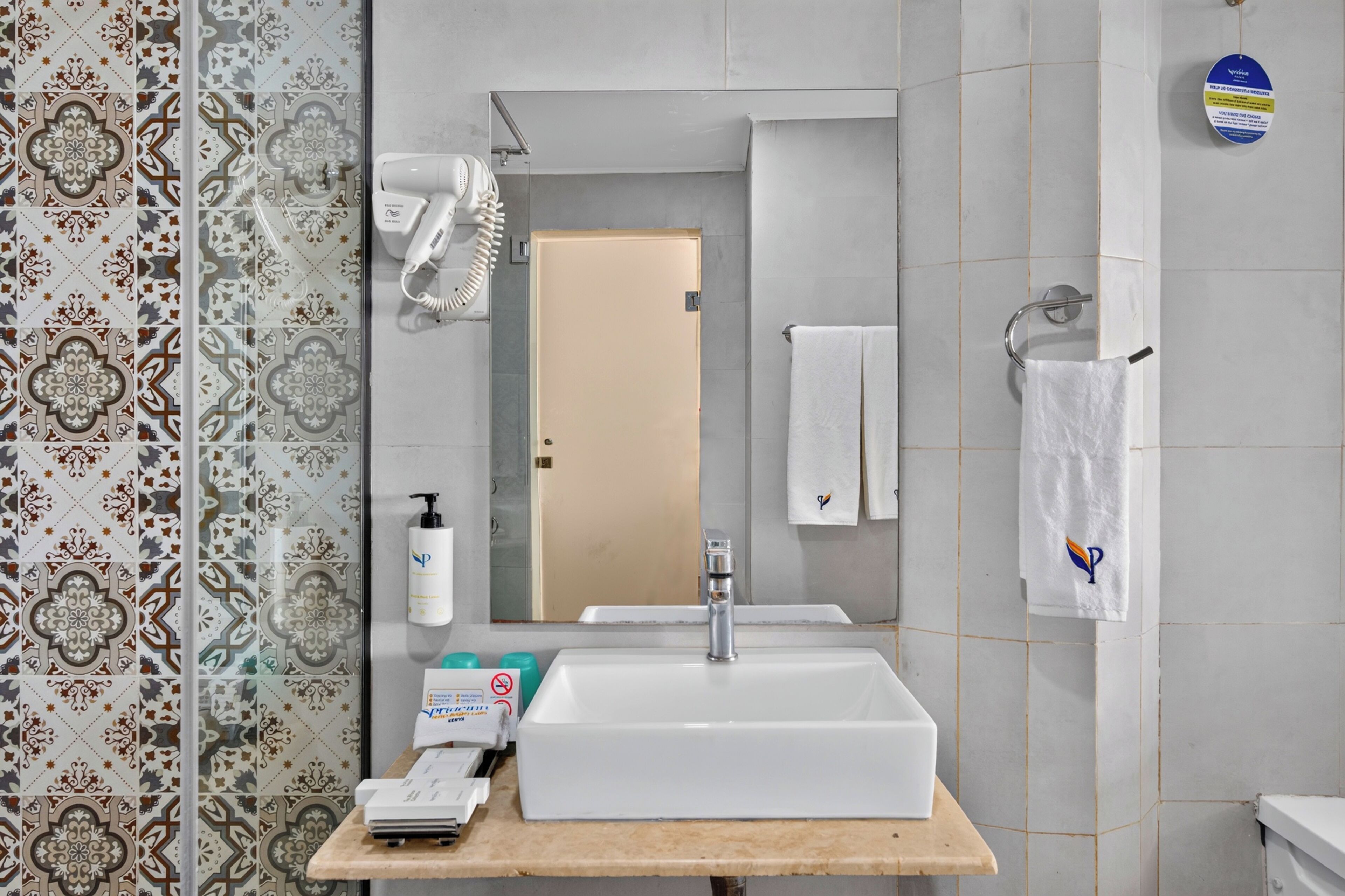 A bathroom with a white sink, a hairdryer, a bottle of shampoo, and a towel rack.