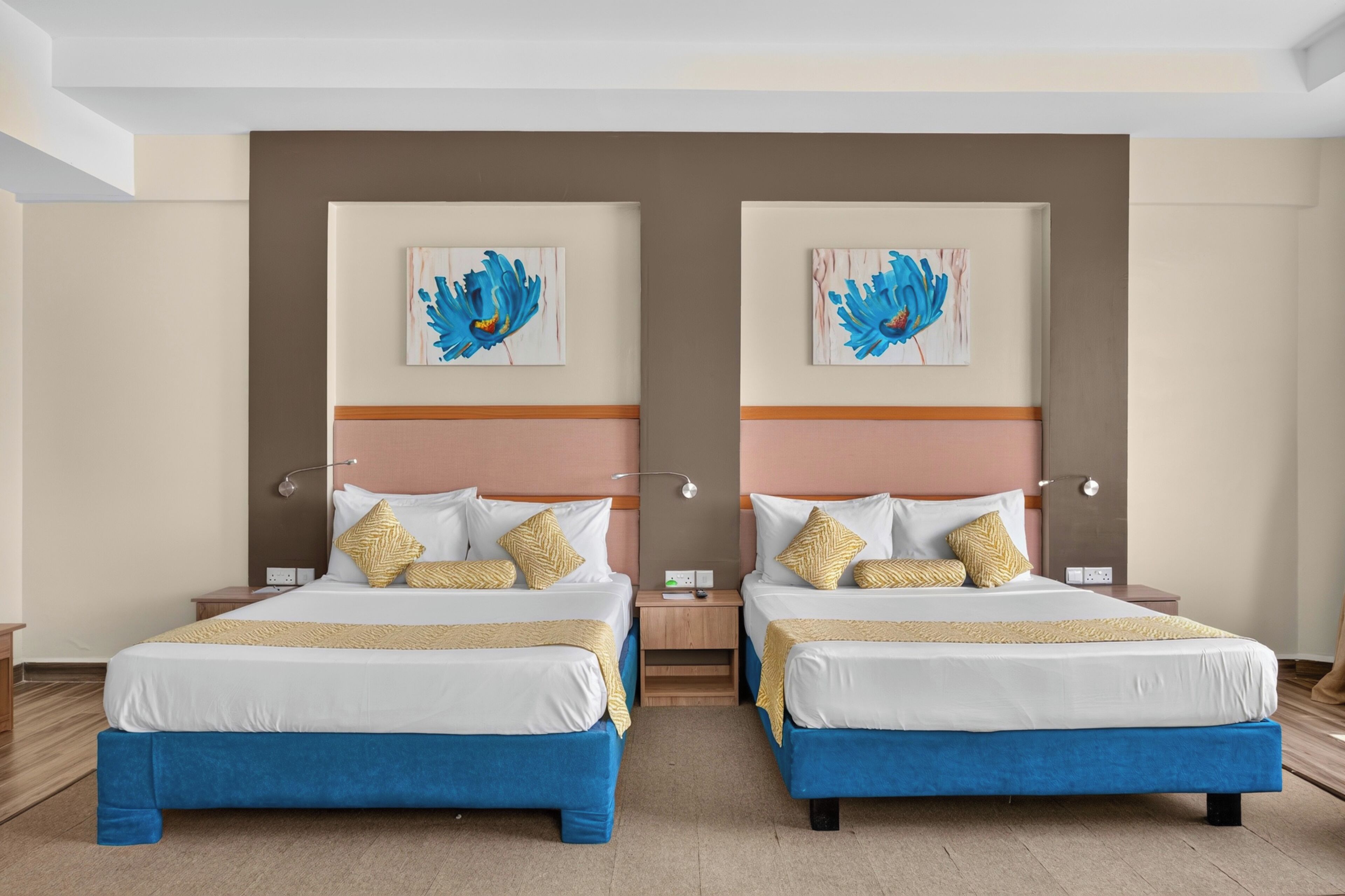 A hotel room with two beds, each with a blue headboard, white bedding, and decorative pillows.