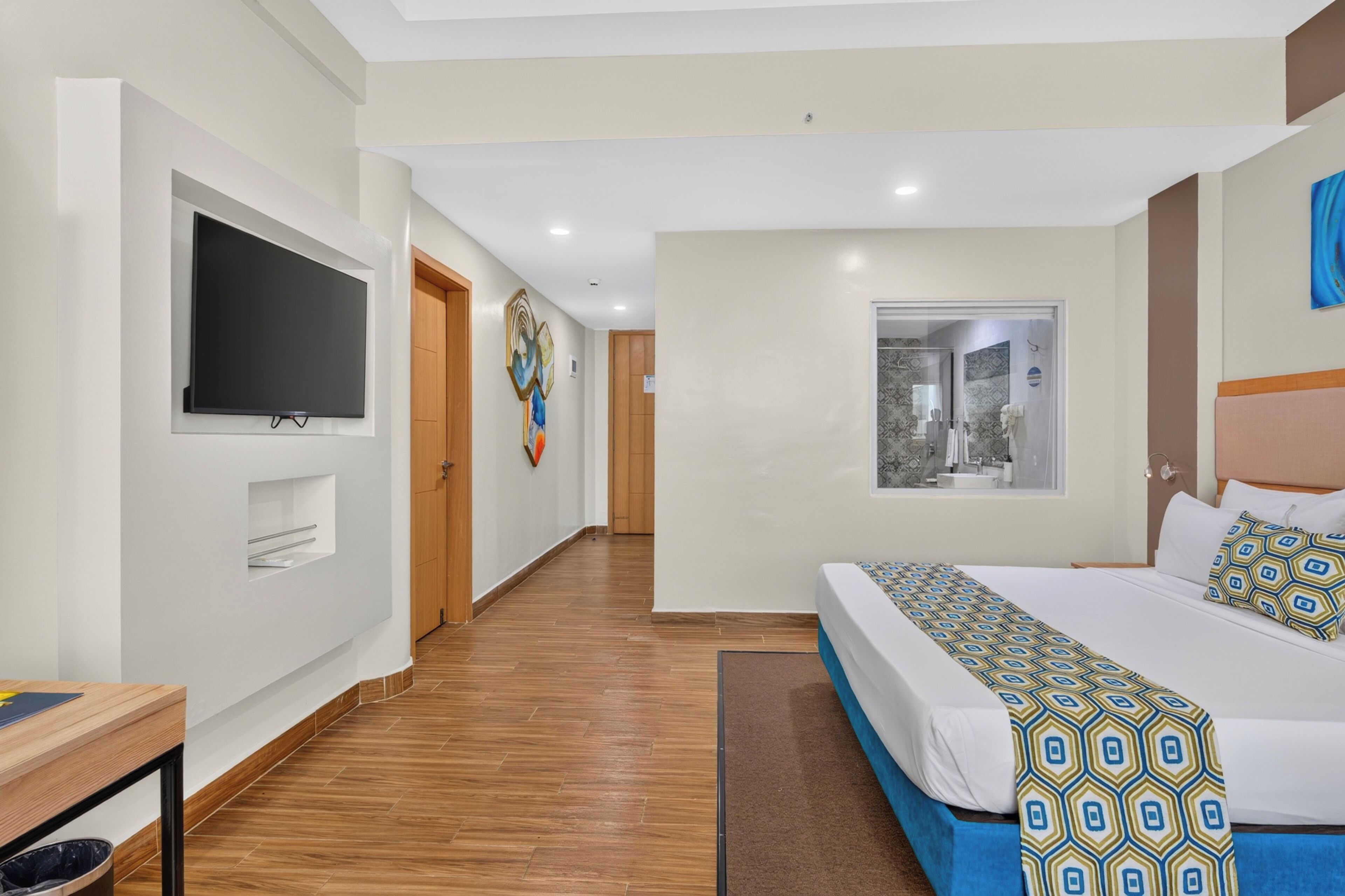 Habitación de hotel con una cama grande, televisor de pantalla plana montado en la pared, piso de madera y ventana con vistas.